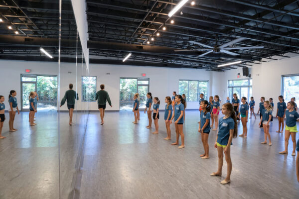 Male dance instructor walking in front of young dancer teaching.